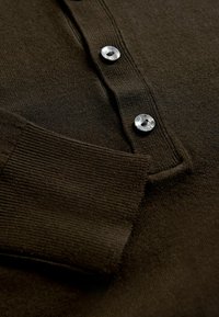 Ciemnobrązowa dzianinowa koszulka polo z prążkowanym kołnierzykiem i dołem, z trzema okrągłymi, błyszczącymi guzikami w jasnym kolorze.