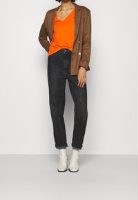 Brunternet blazer, orange v-hals t-shirt, sorte højtsiddende jeans og creme ankelstøvler. Glatte teksturer og tætsiddende silhuet.
