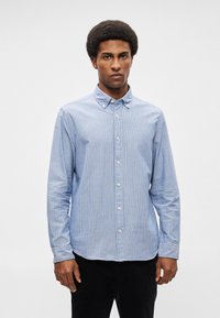 Ριγέ μπλε πουκάμισο με μακριά μανίκια, με γιακά και λευκά κουμπιά. Το ύφασμα φαίνεται μαλακό με λεία υφή.