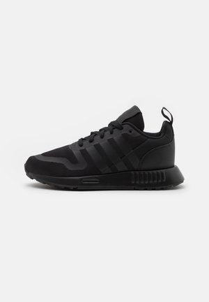 Chaussure de sport basse noire avec tige en mesh, fermeture à lacets, semelle rembourrée et languette au talon, vue de côté extérieur sur fond blanc.