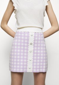 Lila rutmönstrad kjol med en vit vågig midja och en framtida knappstängning med fem runda knappar. Materialet verkar vara strukturerat.