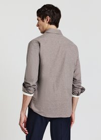 Camicia marrone con trama, colletto, maniche arrotolate e dettaglio sul davanti e sul dietro, abbinata a pantaloni scuri.