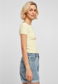 Kortärmad ljusgul topp med rund halsringning, kombinerad med blå denimshorts med uppvikta fållar och två bakfickor.