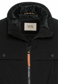 Black jacket with a high collar, featuring a zip closure, leather accent, and a smooth texture. Label reads "camel active."