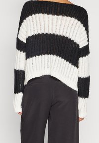 Pull rayé noir et blanc à coupe ample, avec un large col et une texture côtelée. Le dos est raccourci avec des bords effilochés.