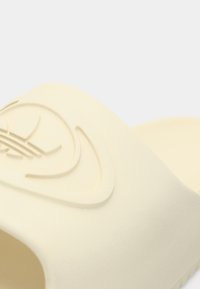 Kremowe klapki na podślizgu wykonane z gładkiego, elastycznego materiału. Posiadają tłoczone logo i profilowaną wkładkę dla wygody.