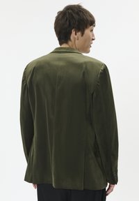 Olivově zelená blazer s hladkým, texturovaným povrchem, s jedním rozventilovaným zadním dílem a klasickými klopami. Obsahuje manžety na knoflíky.