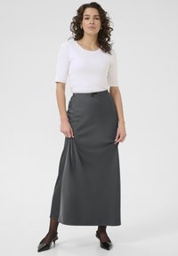 Falda maxi gris con cintura elástica, combinada con una blusa blanca ajustada. Textura suave, diseño hasta el suelo y zapatos negros hasta el tobillo.