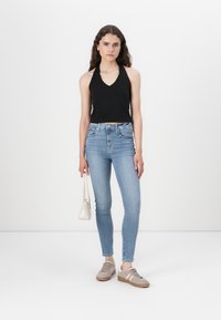 Melna halter top, gaiši zili skinny džinsi, pelēki sporta apavi ar rozā akcentiem un maza balta rokassoma. Gludas tekstūras un pieguļošs dizains.