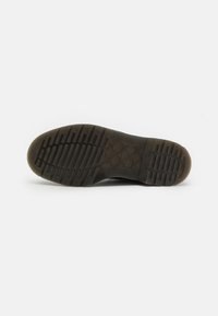 Suola di scarpa in gomma nera con un motivo di presa testurizzato, che presenta linee in rilievo per aderire e un design della punta leggermente arrotondato.