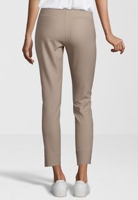 Pantalon beige en tissu texturé avec de petits pois marron, conçu avec une coupe slim et une longueur jusqu'à la cheville, associé à des baskets blanches.