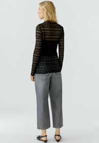 Schwarzes Langarmoberteil mit einer Spitze-Textur und floralem Muster, kombiniert mit lockeren grauen Jeanshosen und schwarzen Ballerinas.