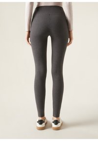 Hochgeschnittene, figurbetonte Leggings aus dunkelgrauem Stoff mit glatter Textur. Verfügt über einen nahtlosen Rücken und wird mit weißen Schuhen und schwarzen Akzenten getragen.