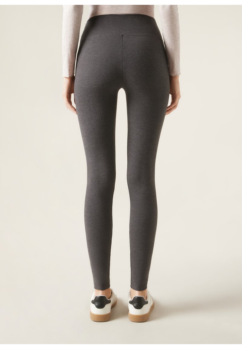 Hochgeschnittene, figurbetonte Leggings aus dunkelgrauem Stoff mit glatter Textur. Verfügt über einen nahtlosen Rücken und wird mit weißen Schuhen und schwarzen Akzenten getragen.