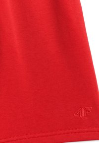 Tissu rouge avec logo "4F" subtilement texturé en relief près du bord inférieur, montrant un détail de couture fine sur l'ourlet.