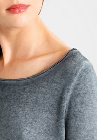 Grå stickad tröja med vid halsringning och mjuk textur, som visar upp en något figursydd silhuett och subtila tonala variationer.