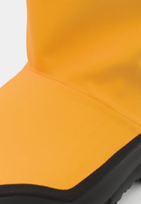 Stivale di gomma giallo con una superficie opaca liscia, un gambale a taglio dritto e una suola nera. Presenta un sottile motivo a quadretti sulla superficie.