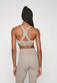 Soutien-gorge de sport beige avec des bretelles croisées dans le dos et un détail en forme de clé. Associé à des leggings beiges taille haute avec des accents de couture.
