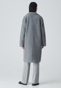 Grau wollene Jacke mit entspannter Passform, Reverskragen und langen Ärmeln. Besitzt eine einzelne Naht auf der Rückseite und wird mit hellgrauen Hosen kombiniert.