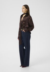 Blusa a fiori scuri con colletto a cravatta, abbinata a jeans in denim blu scuro a gamba larga. La modella indossa scarpe col tacco bordeaux.