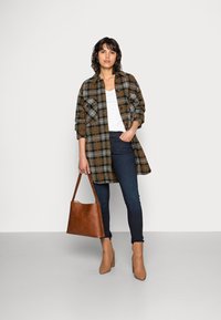 Camisa de cuadros en marrón, verde y naranja, combinada con una blusa blanca, vaqueros oscuros y botines de tacón en color beige. Se incluye un bolso tote marrón.