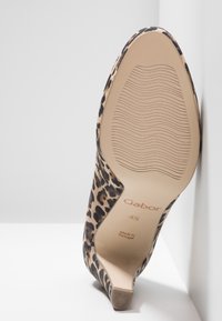 Chaussure à talon haut imprimé léopard avec une tige en daim texturé, un bout pointu et une semelle beige lisse présentant un motif ondulé subtil.