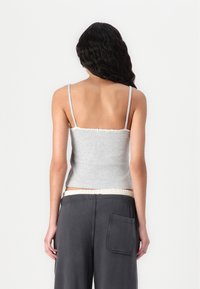 Šedý pletený crop top s tenkými ramínky, řaseným výstřihem a přiléhavým střihem, v kombinaci s volně padnoucími tmavě šedými kalhotami s zadní kapsou.