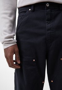 Ciemnoniebieskie spodnie wykonane z wytrzymałego materiału, z dwoma przednimi kieszeniami ozdobionymi miedzianymi elementami oraz prostym krojem.