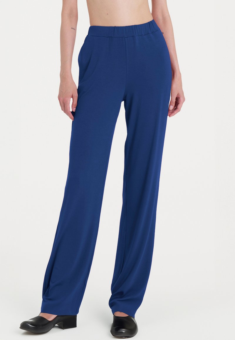 Pantaloni blu a gamba larga realizzati in un tessuto morbido con vita elasticizzata. Indossati con scarpe nere con tacco grosso.