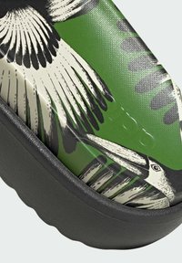 Green slip-on shoe featuring a bird print design with textured black rubber sole and contrasting graphic elements on the surface.