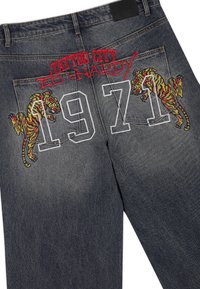 Jeans in denim grigio scuro con tigri ricamate sulle tasche posteriori, testo rosso "Tattoo City Ed Hardy" e grandi numeri bianchi "1971" sovrapposti alle tasche.