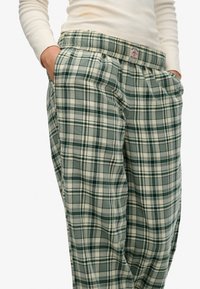 Pantalon à carreaux verts en tissu doux, doté d'une coupe décontractée, d'une taille élastique, de poches latérales et d'un motif avec des accents blancs.