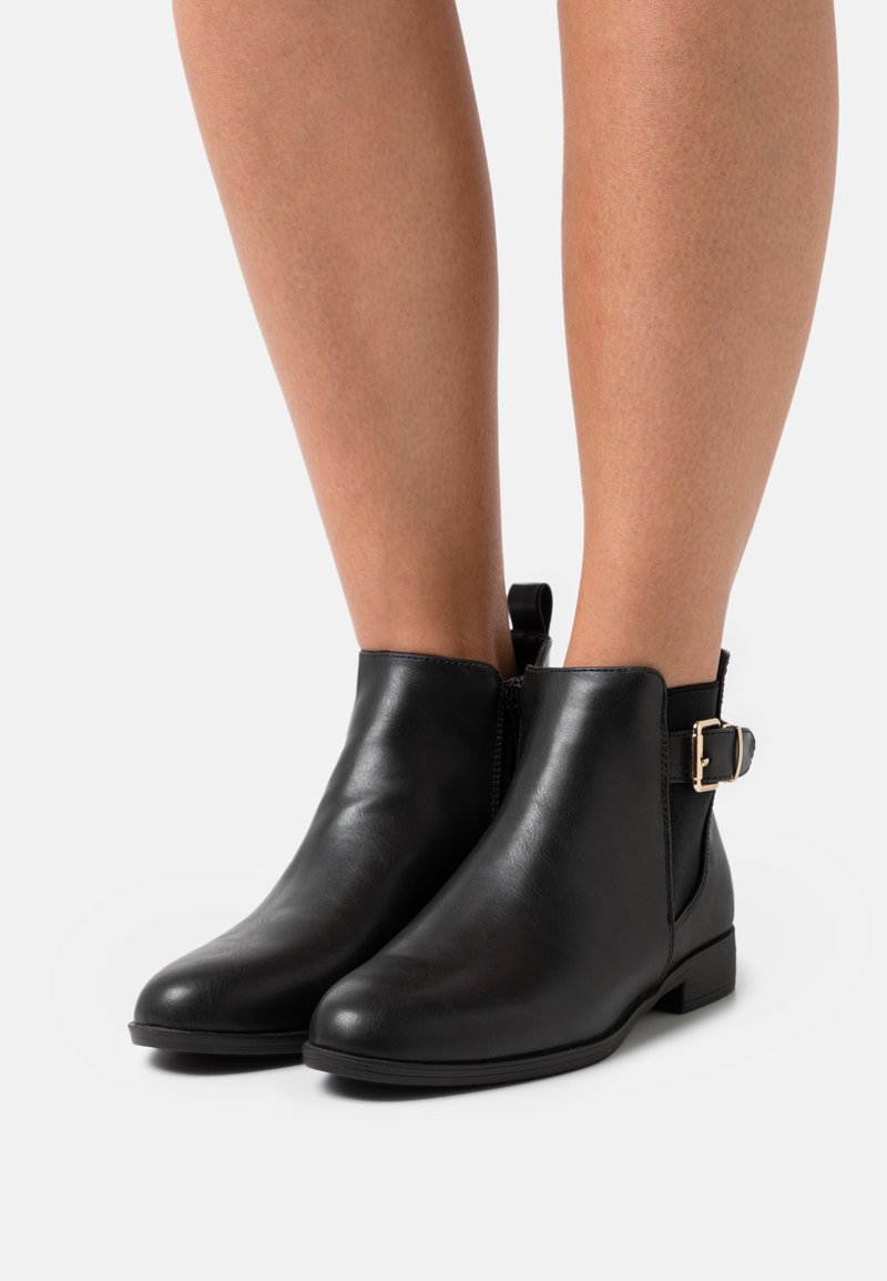 Bottines en cuir noir, avec un bout arrondi, des panneaux élastiques sur les côtés, une languette à l'arrière, et un détail de boucle dorée sur le côté.