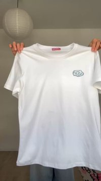 Λευκό T-shirt Diesel που κρατιέται από χέρια, με μικρό γκρι λογότυπο στο αριστερό στήθος, απλό φόντο με κρεμαστό στρογγυλό χάρτινο φανάρι.
