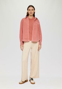 Lichtroze corduroy overhemd, gestructureerd oranje gebreid trui, beige wijde broek en sneakers met een patroon en een bruine Zool. Eenvoudige, casual outfit.