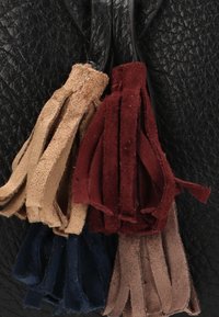 Bolso de cuero negro texturizado que presenta cuatro borlas de ante en colores beige, burdeos, azul marino y marrón, añadiendo detalle y contraste.