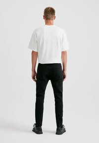 Camiseta blanca de manga corta combinada con jeans negros ajustados y zapatillas negras, mostrando un diseño sencillo y un contraste de colores clásico.
