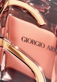 Giorgio Armani parfumburk med en böjd gyllene detalj, rosa glasbehållare och graverad svart logotyp. Slät yta med reflekterande ytor.