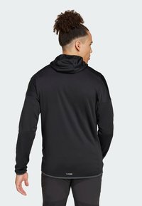 Black long-sleeve hoodie with a smooth texture, fitted design, and a hood. Features contrasting accents and a subtle logo near the hem.