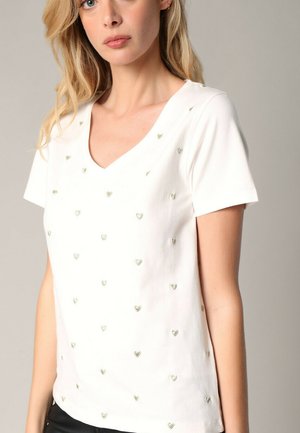 T-shirt blanc à manches courtes et col en V, arborant de petits cœurs brodés de couleur métallique répartis uniformément sur le tissu.