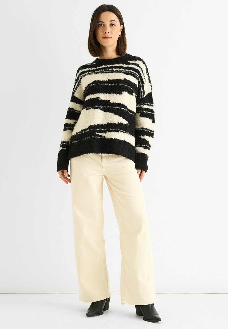 Schwarzer und cremefarbener gestreifter Strickpullover mit lässiger Passform, langen Ärmeln und gerippten Bündchen, kombiniert mit cremefarbenen, hochgezogenen, weiten Hosen.