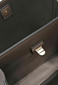 Intérieur en cuir noir d'un sac à main avec une texture lisse, présentant un fermoir doré et un détail de marque sur un panneau latéral.