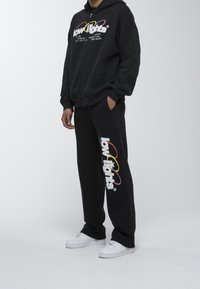 Conjunto de sudadera negra con capucha y pantalones con el logo "low lights" en texto colorido. Hecho de tela suave, con bolsillos laterales y zapatillas blancas.