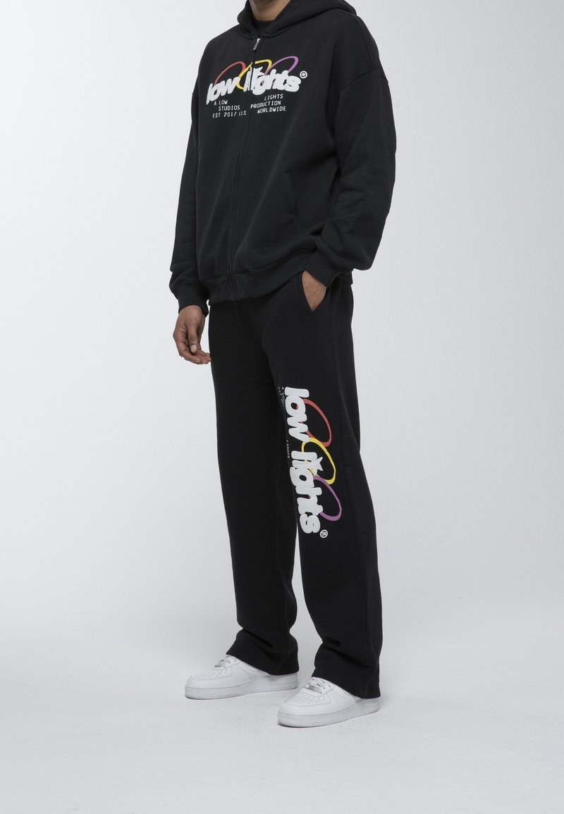Conjunto de sudadera negra con capucha y pantalones con el logo "low lights" en texto colorido. Hecho de tela suave, con bolsillos laterales y zapatillas blancas.