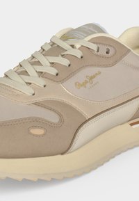 Μπεζ και κρεμ sneaker Pepe Jeans με κορδόνια, υφή στην σόλα και το όνομα της μάρκας τυπωμένο στο πλάι και στη γλώσσα.