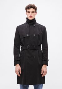 Mustast topeltrinnalisest esitusega trentsmantlist, kõrge krae, reguleeritava vöökohaga ja nööpidega varrukasuu. Sile kangas, struktuurse lõikega.