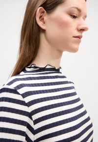 Marineblau-weiß gestreifte Bluse mit gerippter Textur und Rüschendetail am Kragen, seitlich betrachtet, mit taillierter Silhouette.