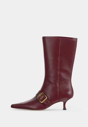 Botte en cuir bordeaux mi-mollet avec bout pointu, détail de bride à boucle dorée et petit talon kitten heel.