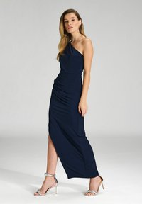 Robe maxi bleu marine à une épaule avec fronces, dotée d'une fente haute sur la cuisse. Accompagnée de sandales à talons hauts argentées à lanières.