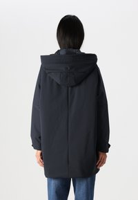 Parka étanche bleu marine foncé avec une capuche, coupe décontractée, détail bouton au niveau du cou et poignets élastiques. Texture lisse avec des coutures minimales.